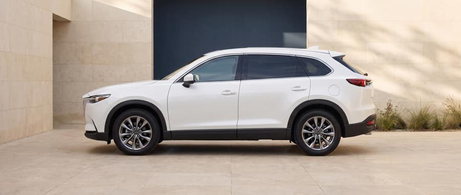 Side profile of the white 2021 Mazda CX-9 in a warm-stone architectural setting