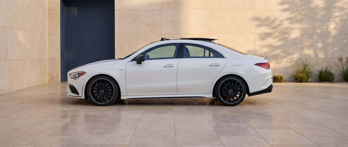 Side profile of the white 2022 Mercedes-AMG CLA 35 in a warm-stone architectural setting