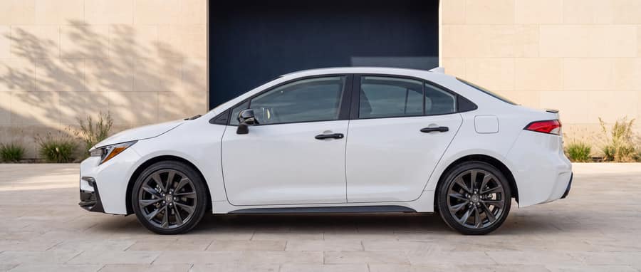 Side profile of the white 2023 Toyota Corolla Hybrid SE in a warm-stone architectural setting
