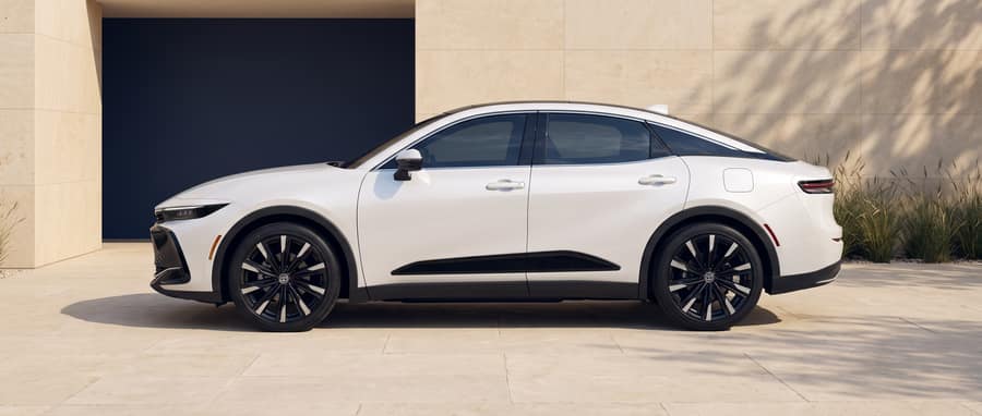 Side profile of the white 2024 Toyota Crown in a warm-stone architectural setting