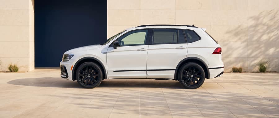 Side profile of the white 2021 Volkswagen Tiguan in a warm-stone architectural setting
